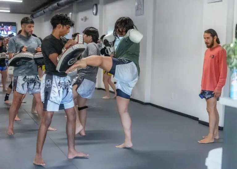 Students practicing Muay Thai kick drills with focus pads during martial arts class at training gym.
